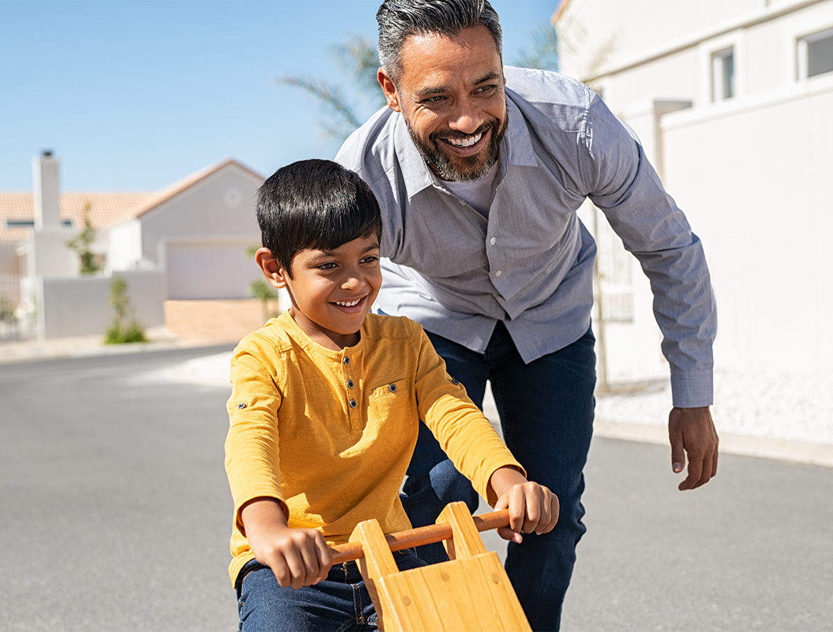 Father pushing son on toy smiling